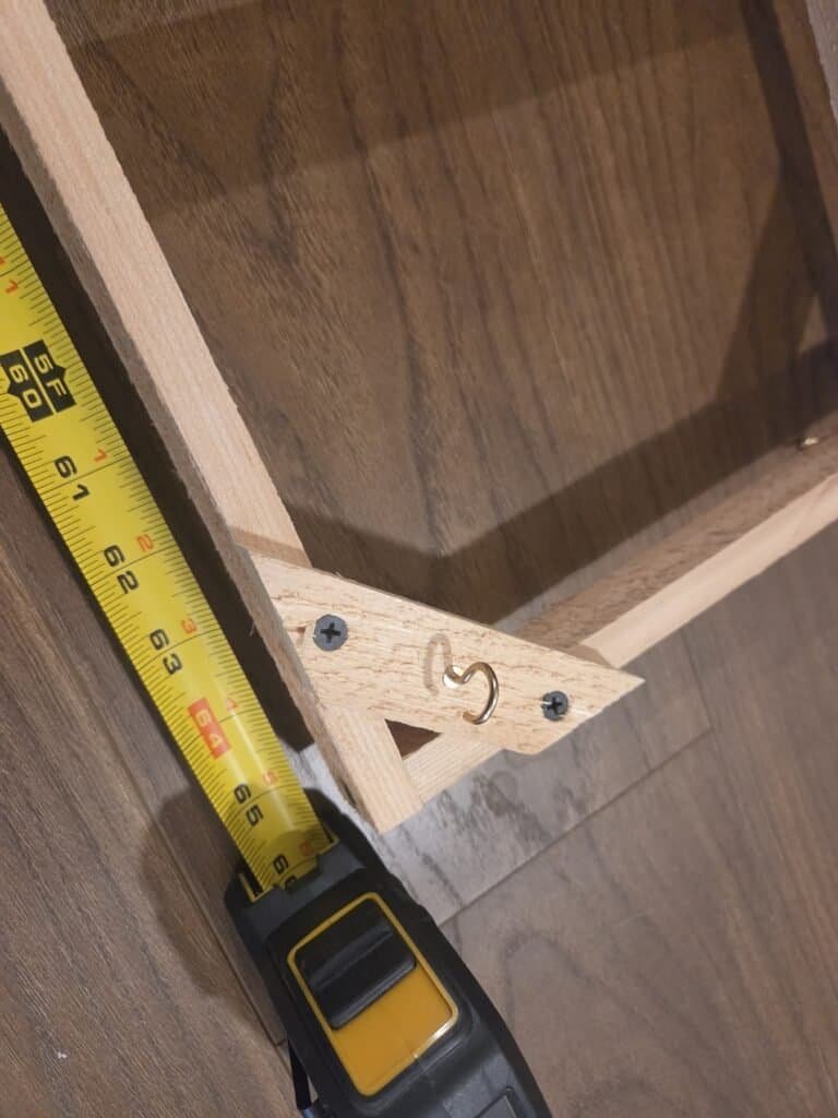 Close-up of a diagonal corner brace with a brass screw hook, tape measure alongside