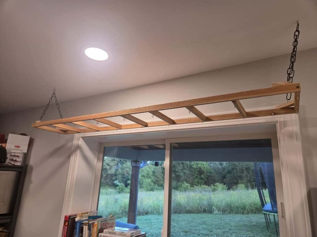 Empty cedar herb rack freshly hung on chains over a window at dusk, before bundles were added